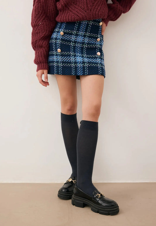 Zbliżenie na nogi modelki ubranej w mini spódniczkę w granatową kratę DISSA , podkolanówki SCHOOLI i buty lesotho.