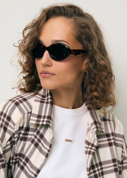 Zbliżenie na modelkę w brązowych okularach ENNA, białym T-shircie TISHALLE oraz w koszuli w kratę FALBI.