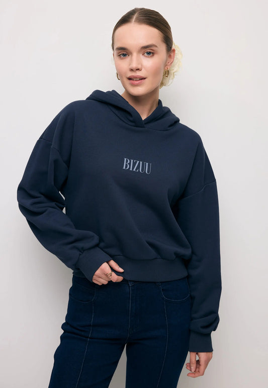 Zbliżenie na modelkę w granatowej bluzie z kapturem i niebieskim logo na przodzie SAY.