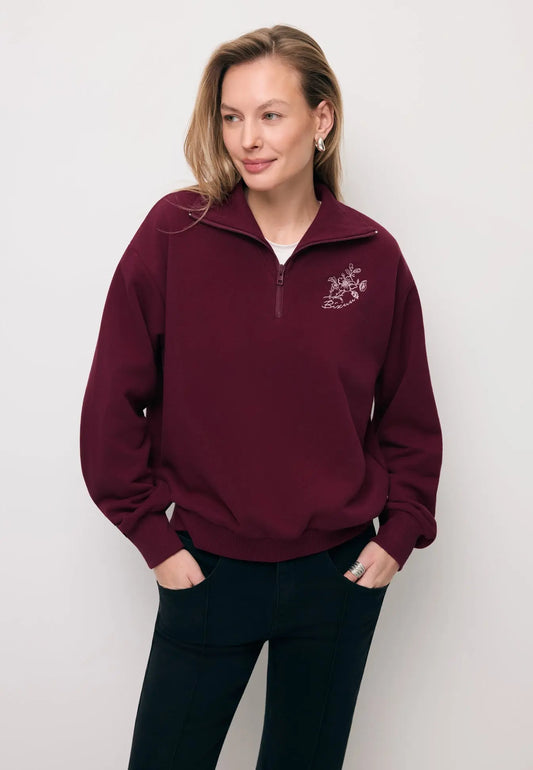 Modelka z rękoma w kieszeni spodni ubrana w bordową bluzę typu half-zip TANSY.
