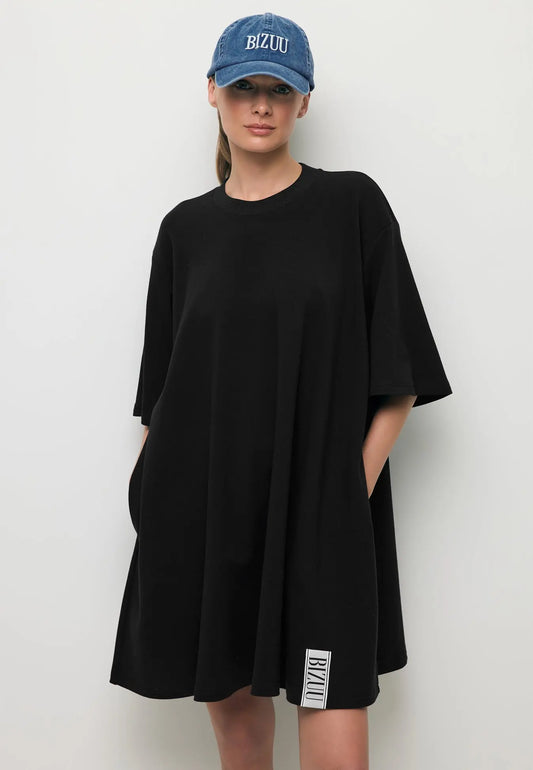 Zbliżenie na modelkę w mini dzianinowej sukience TRESS ozdobną logowaną metką oraz niebieską czapką z daszkiem ZANE.