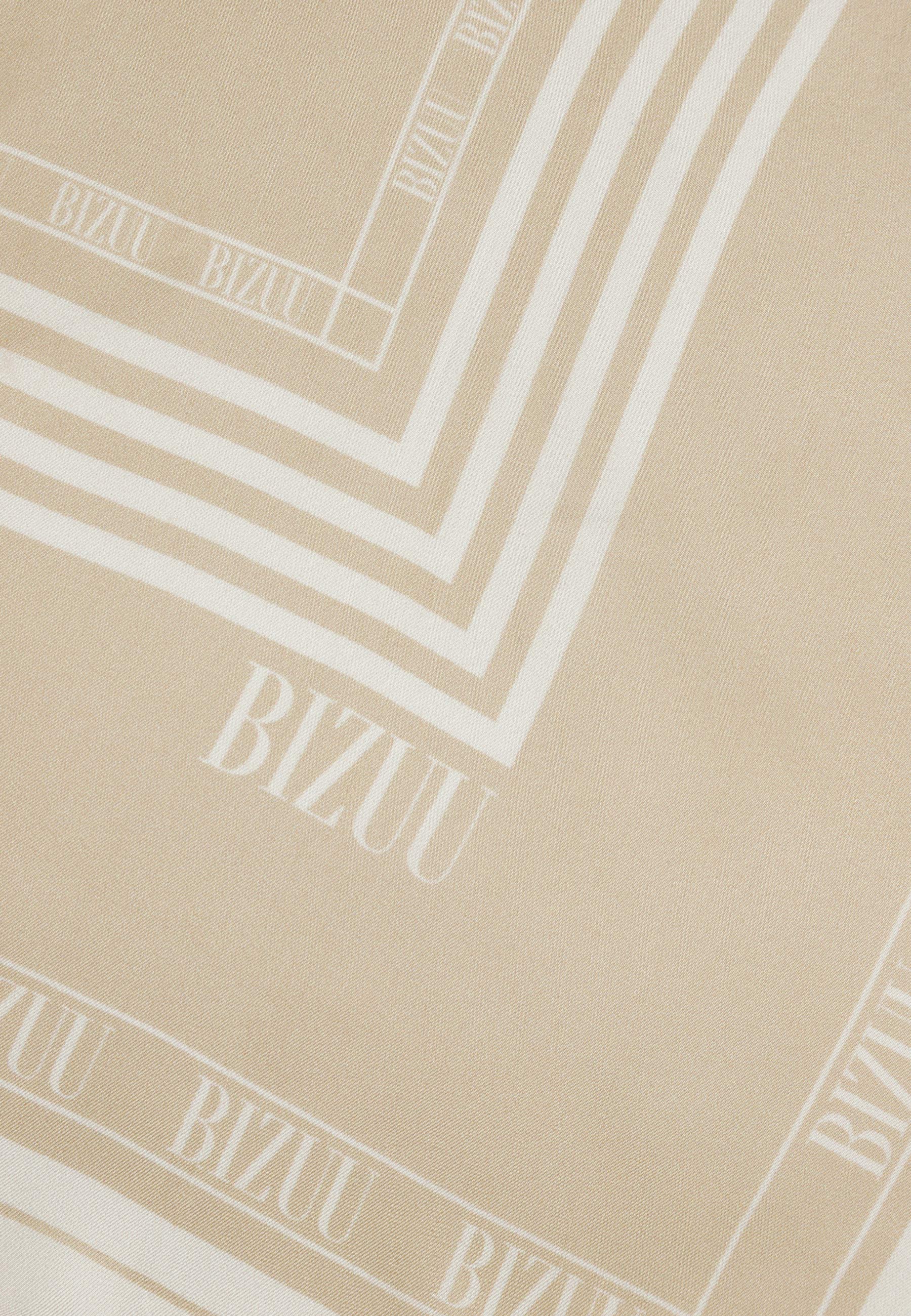 Zbliżenie na logo na beżowej, jedwabnej apaszce ARIA.