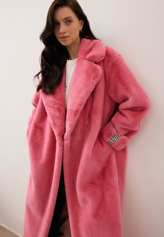 Modelka oparta o ścianę w różowym płaszczu futrzanym DOLOMITES o kroju oversize z ozdobną metką na rękawie.