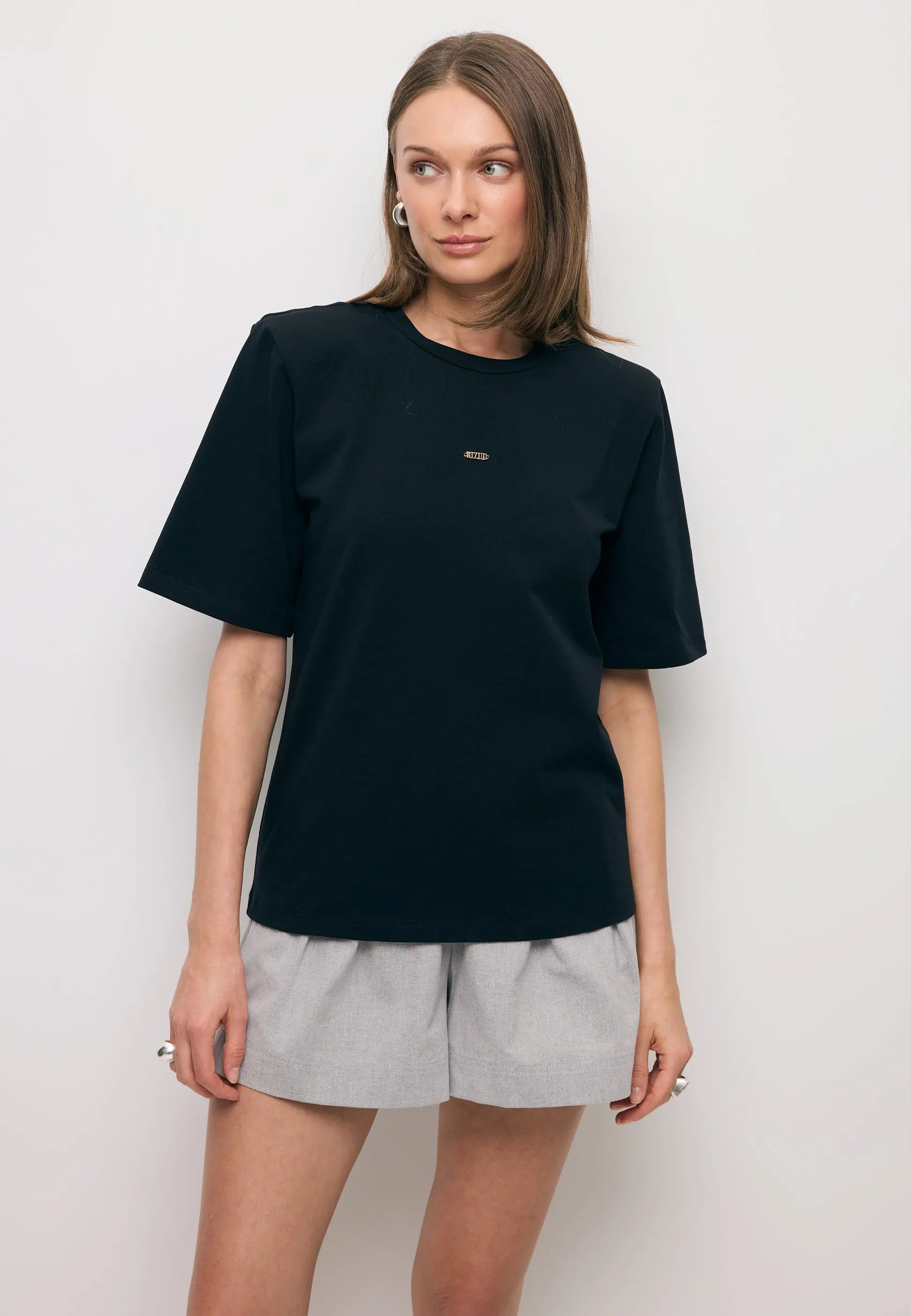 Modelka patrząca w bok ubrana w czarny T-shirt MELISA z poduszkami na ramionach.