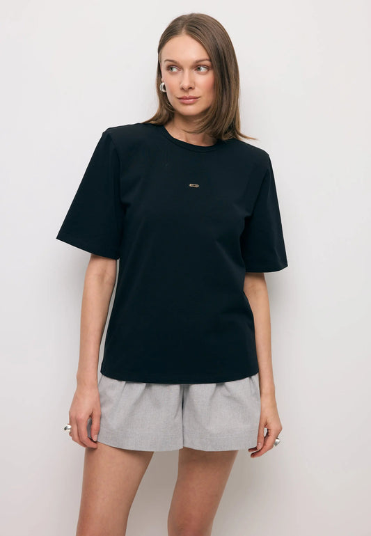 Modelka patrząca w bok ubrana w czarny T-shirt MELISA z poduszkami na ramionach.