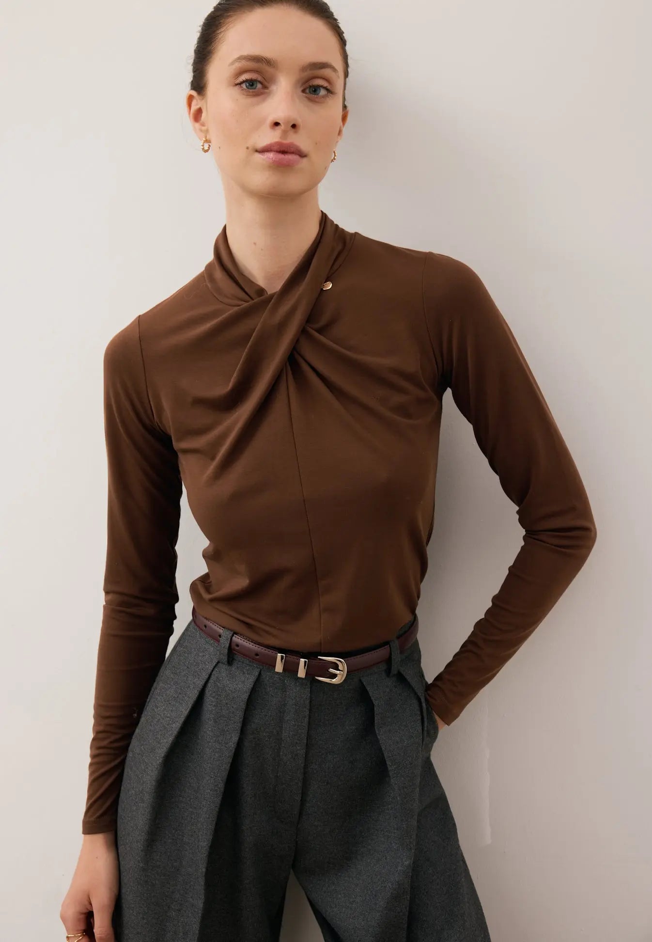 Zbliżenie na modelkę z jedną ręką z tyłu ubraną w czekoladowy longsleeve z przepleceniem PINOWA oraz szerokie spodnie BANOS.