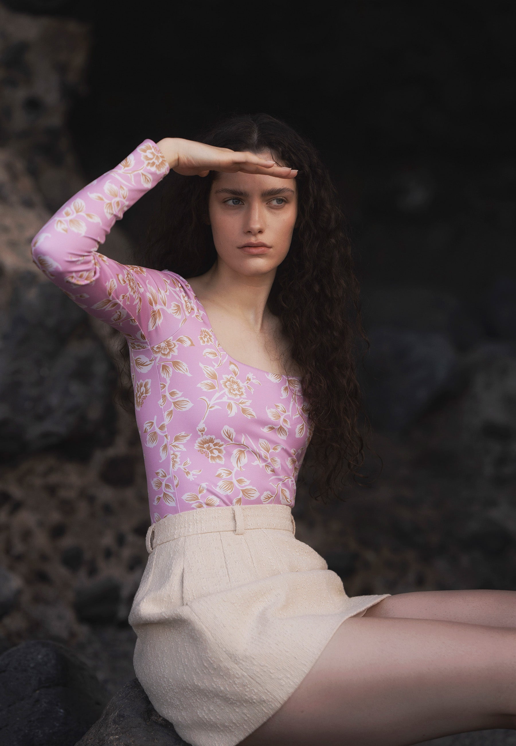 Modelka siedząca na skale ubrana w różowe body w kwiatowy print SANDY oraz beżową spódniczkę BREDA.