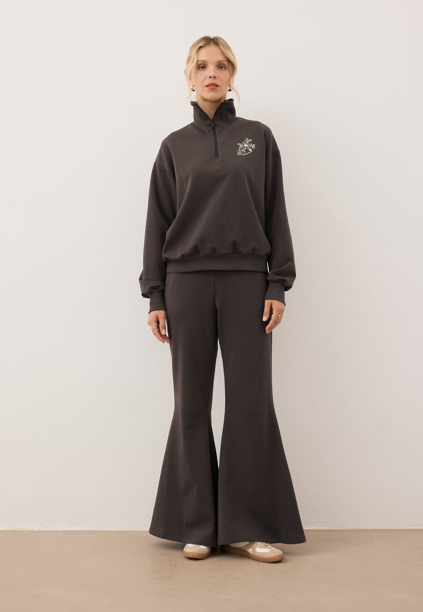 Modelka ubrana w czekoladowy dres z bluzą half zip TANSY i spodniami z szerokimi nogawkami ZEIA.