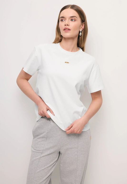 Zbliżenie na modelkę ubraną w biały t-shirt TISHAL ze złotym logo na przodzie.