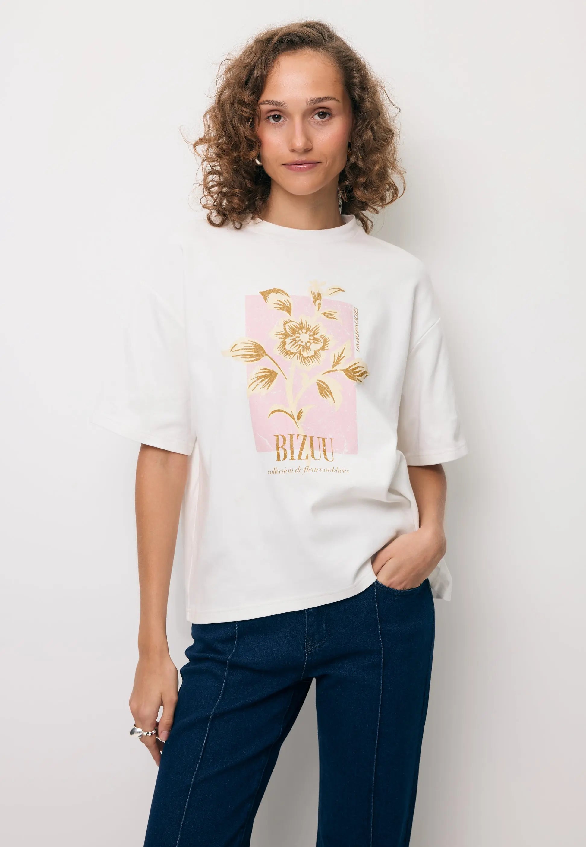 Modelka z ręką w kieszeni granatowych spodni BELINNA, ubrana w kremową koszulkę z autorską grafiką VIORA.