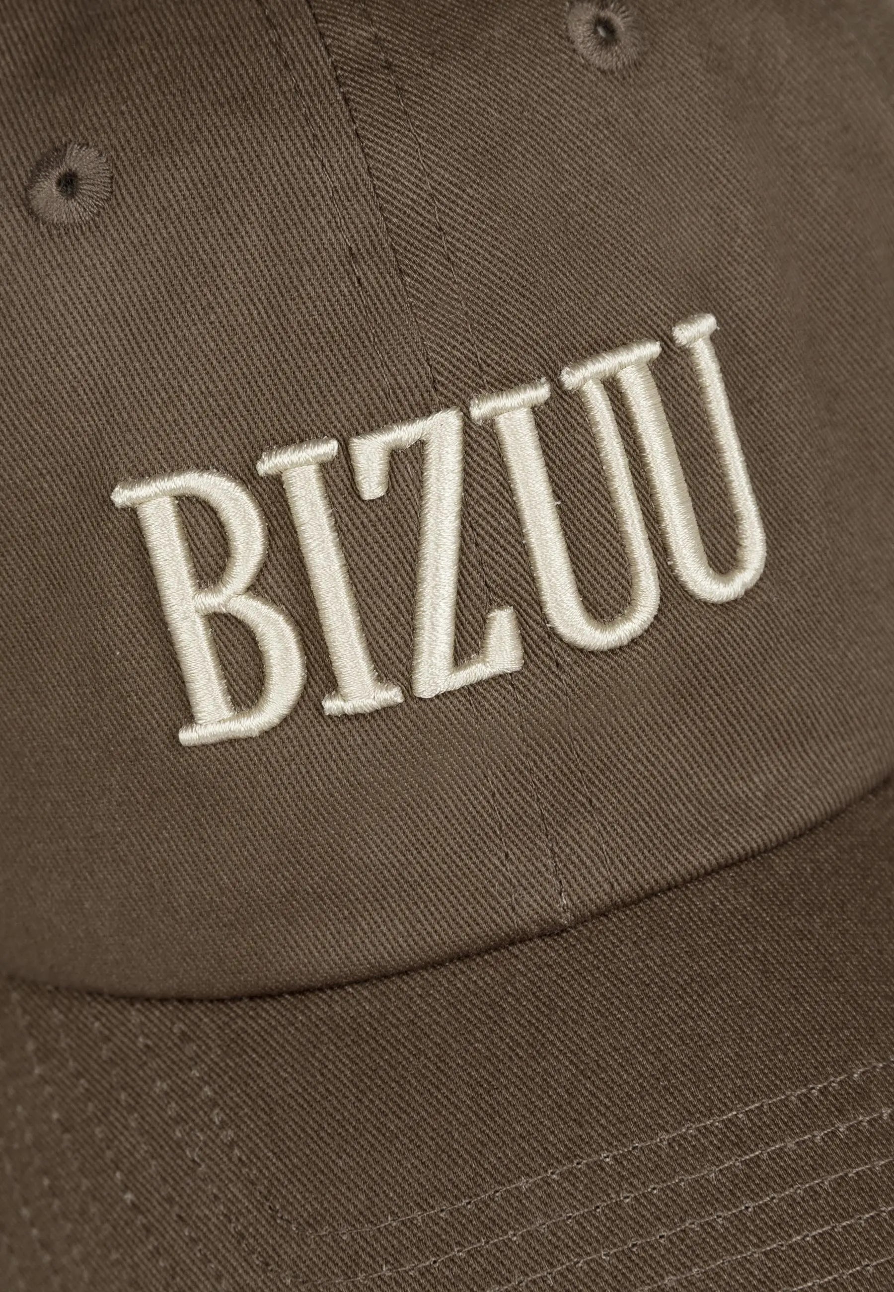 Zbliżenie na logo haftowane na przodzie czapki z daszkiem ZANE w kolorze brązowym.