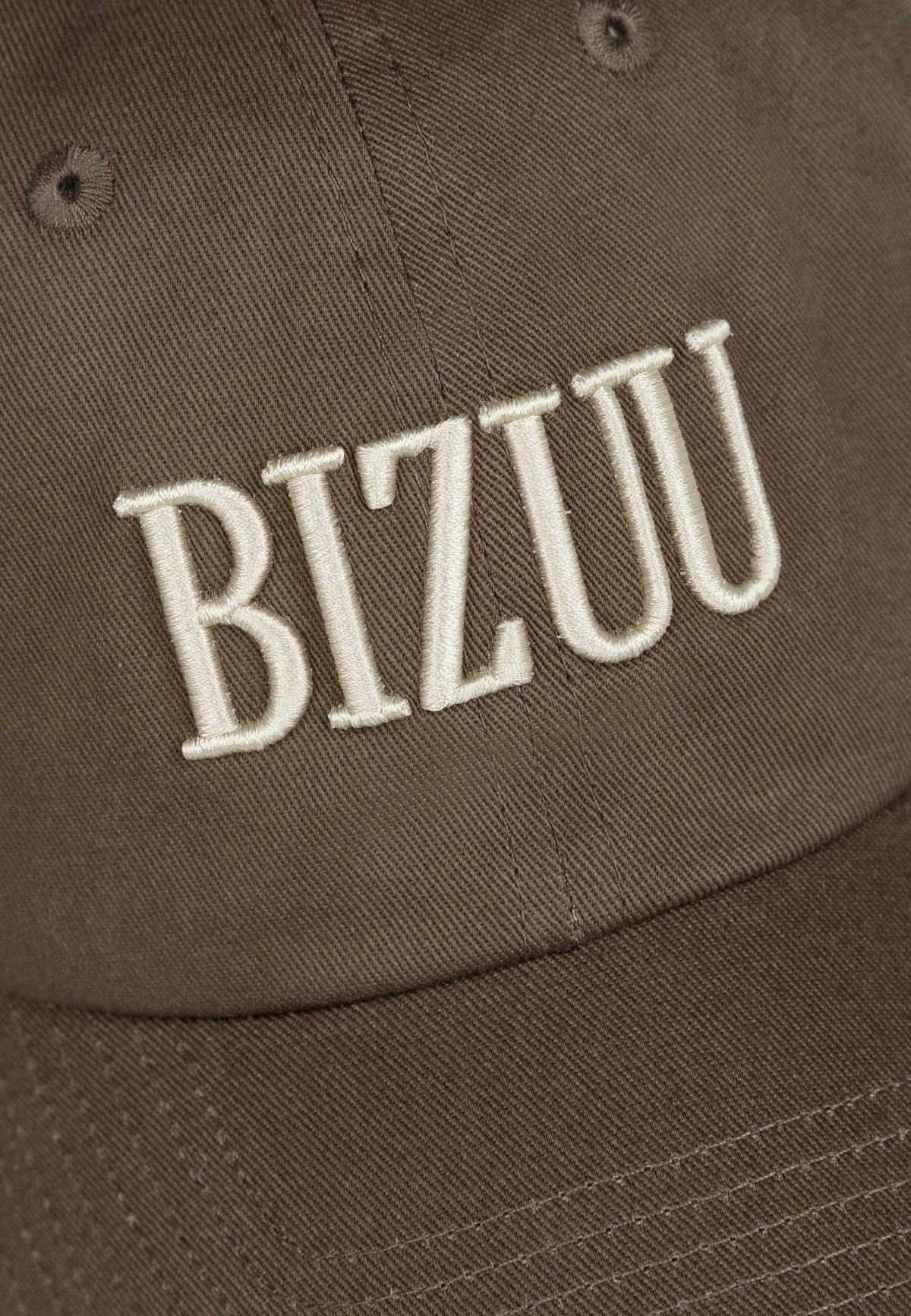 Zbliżenie na logo haftowane na przodzie czapki z daszkiem ZANE w kolorze brązowym.